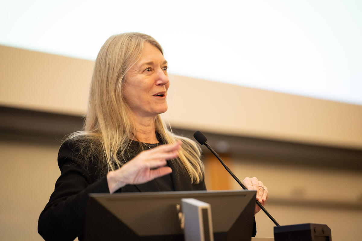 Cori Bargmann giving a talk in front of a microphone, smiling and gesturing with her hands.