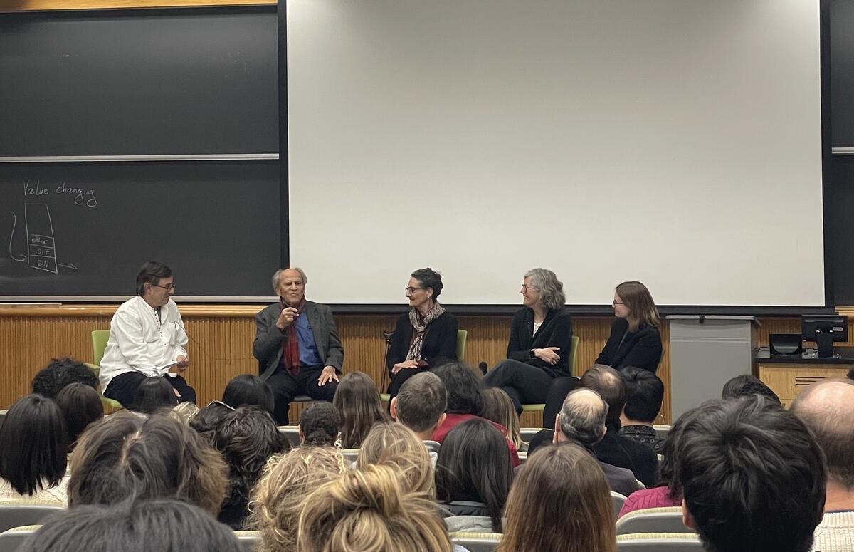 Isacoff, Wiesel, Shatz, Feller, and Vlasits are seated in front of an audience in a lecture hall. Wiesel is speaking and the other panelists are looking at him.