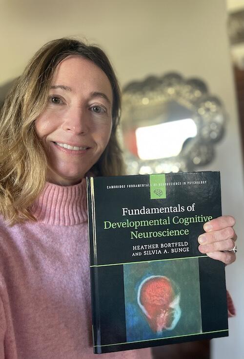 Silvia Bunge smiling, holding a textbook titled “Fundamentals of Developmental Cognitive Neuroscience” by Heather Bortfeld and Silvia A. Bunge.